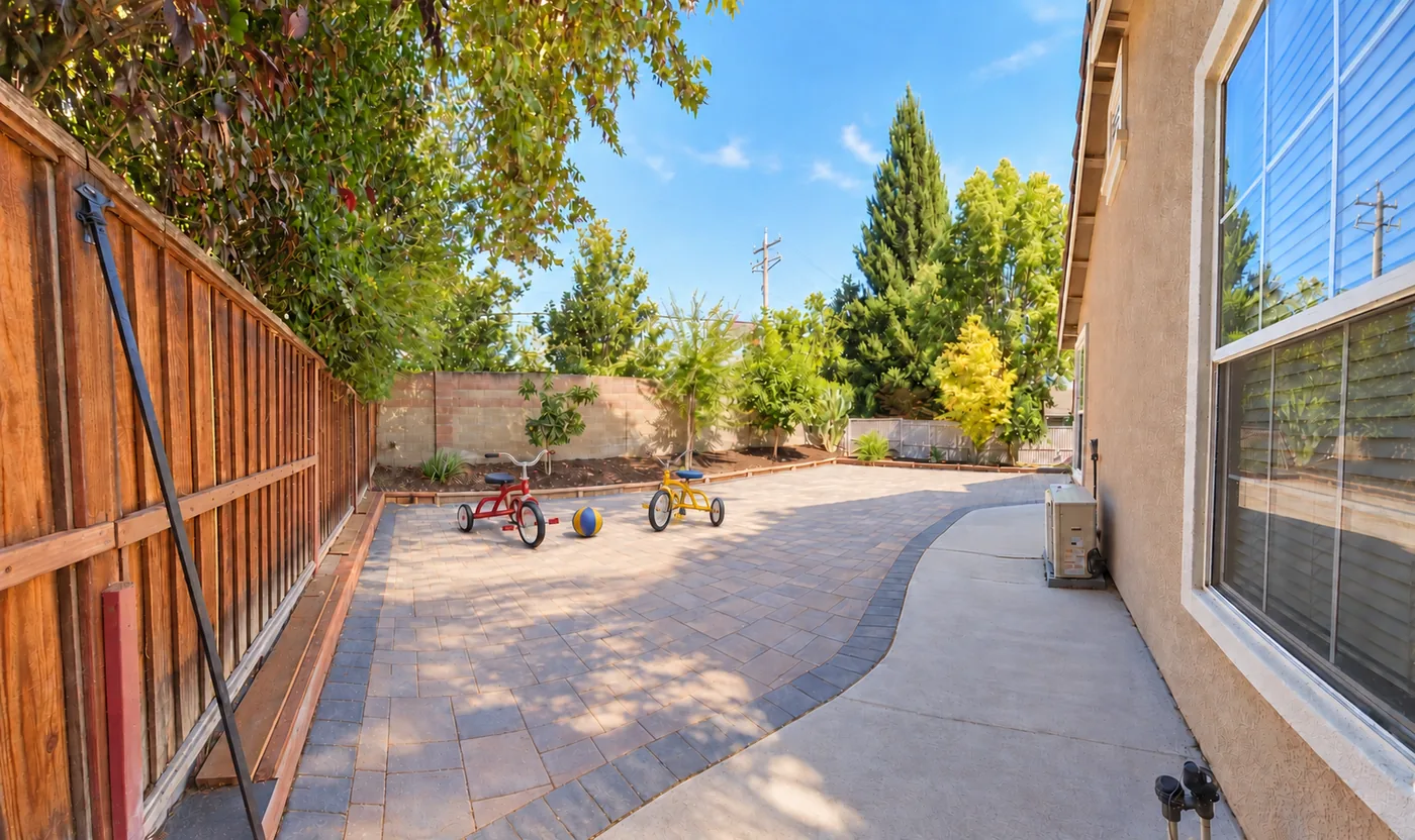 Enclosed side yard path at Lia's Preschool with tricycles and ball on a paver walkway